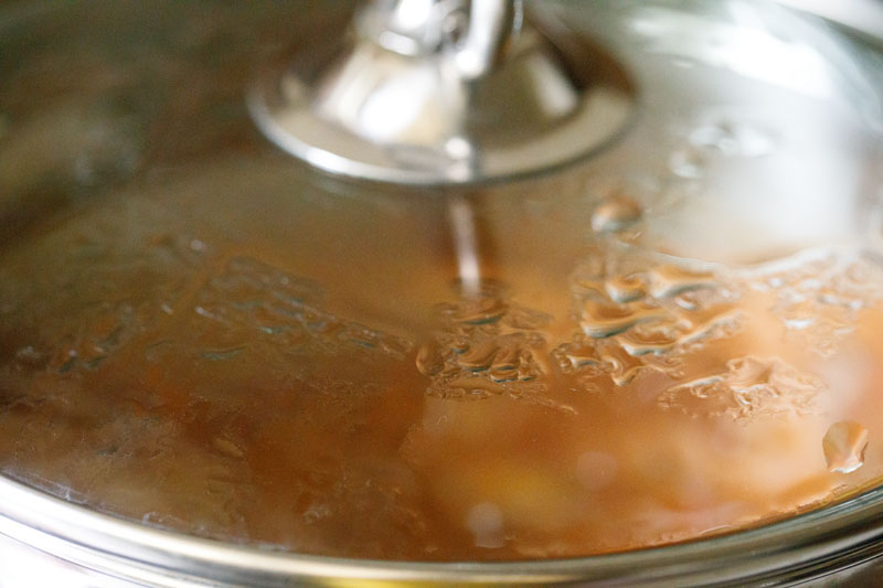 lid on stock pot with veggies simmering in tomato broth