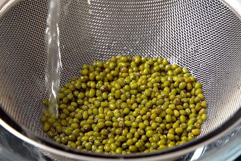 green gram or mung beans being rinsed in water in a mesh strainer