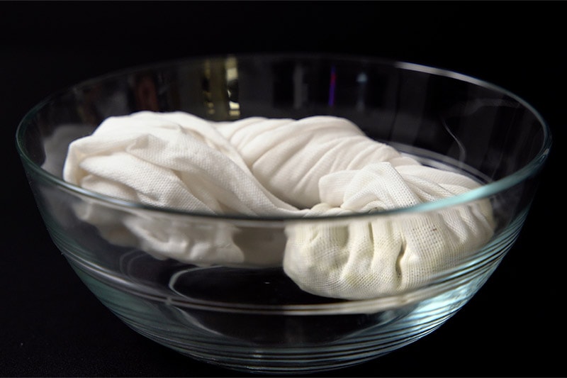 folded white cotton napkin with mung beans inside it placed in a glass bowl