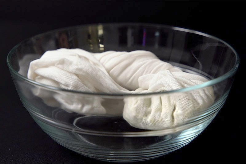 folded white cotton napkin with mung beans inside it placed in a glass bowl