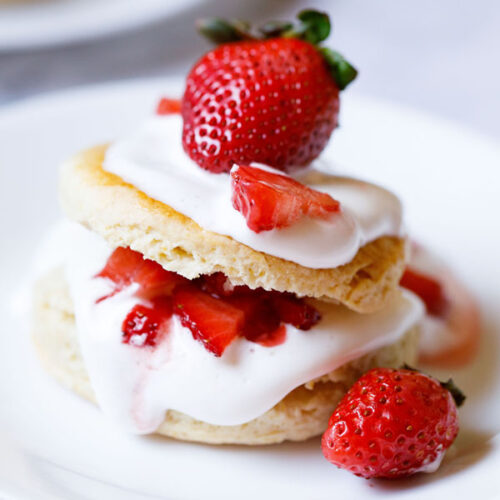 strawberry shortcake with the cream and strawberry filling seen and topped with some and a large strawberry on top on a white plate