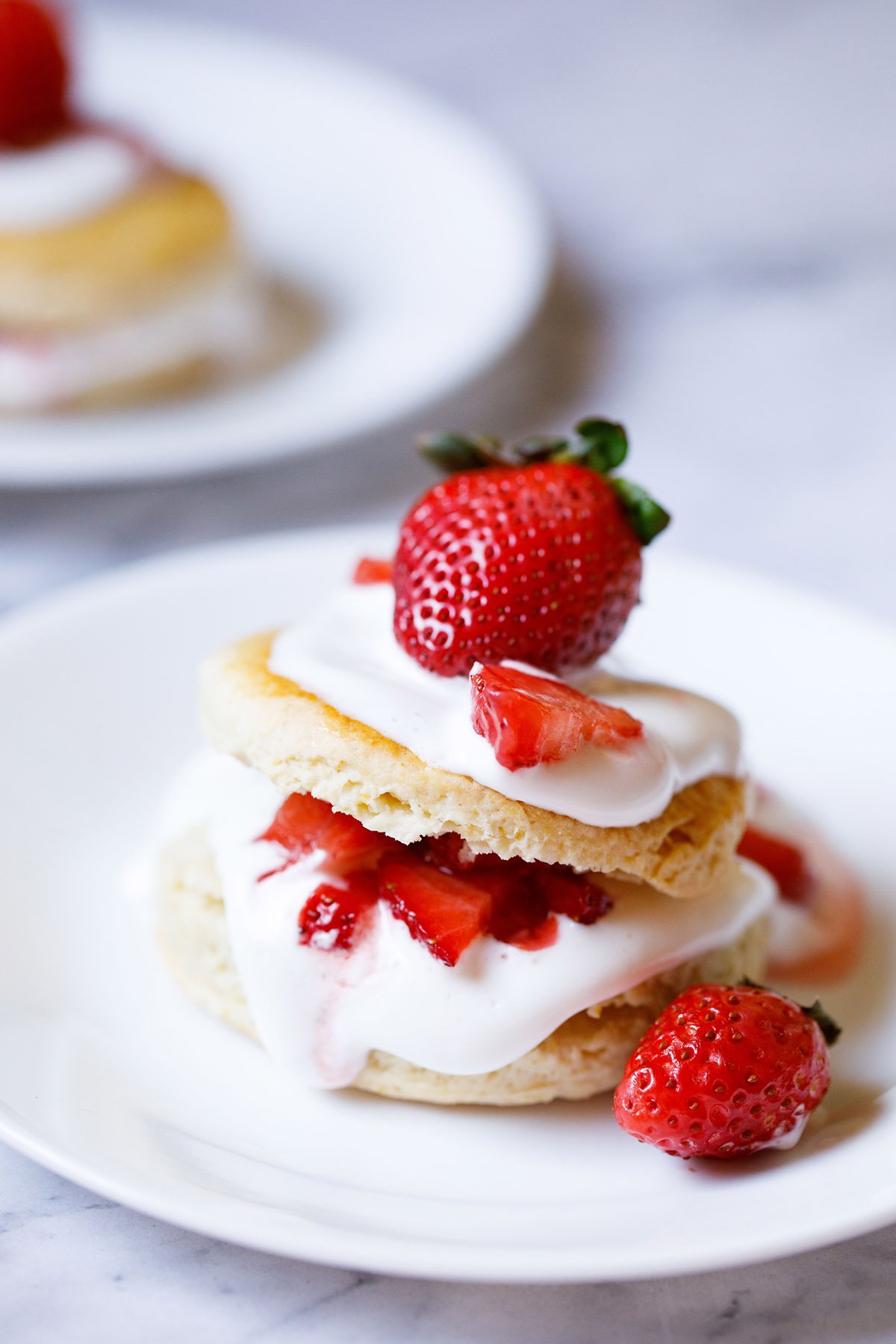 strawberry shortcake with the cream and strawberry filling seen and topped with some and a large strawberry on top on a white plate