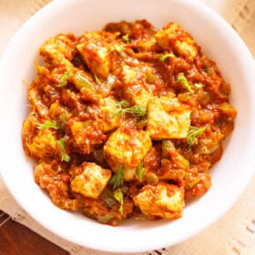 overhead shot of tawa paneer with coriander leaves garnish in a white bowl on a cream linen