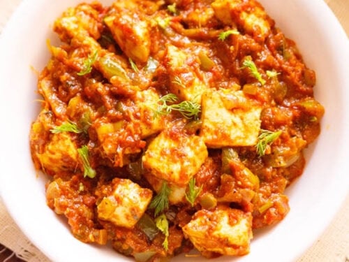 overhead shot of tawa paneer with coriander leaves garnish in a white bowl on a cream linen