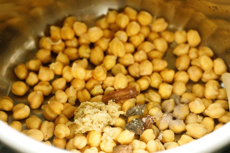 adding ginger paste, whole spices, black salt and dried amla pieces to the chickpeas in a pressure cooker. 