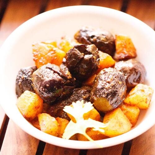 bharwa baingan with potatoes in a white bowl with a coriander sprig on a wooden tray