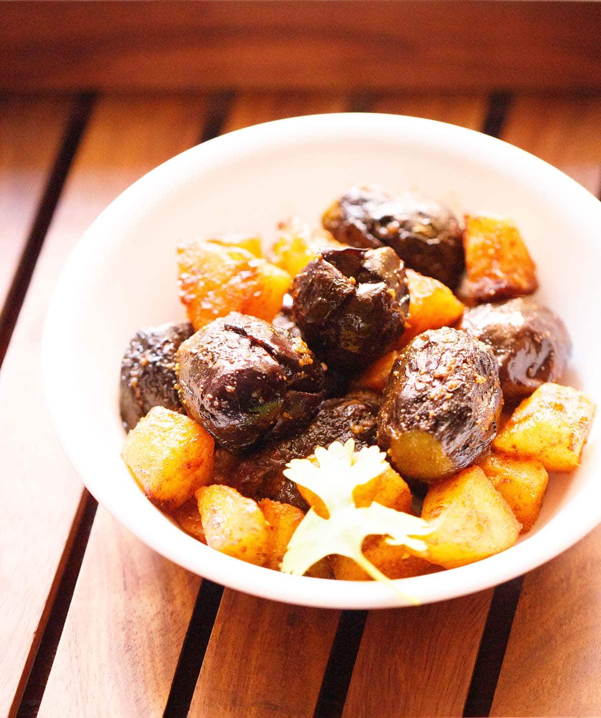 bharwa baingan with potatoes in a white bowl with a coriander sprig on a wooden tray