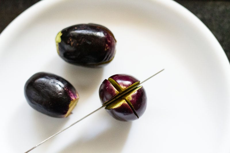 baby aubergines being given a cut with a knife on a white plate