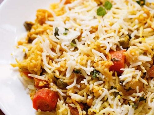 close up shot of biryani on white plate on wooden table