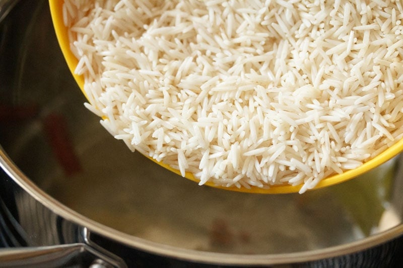 Soaked white rice being poured from yellow bowl into pot