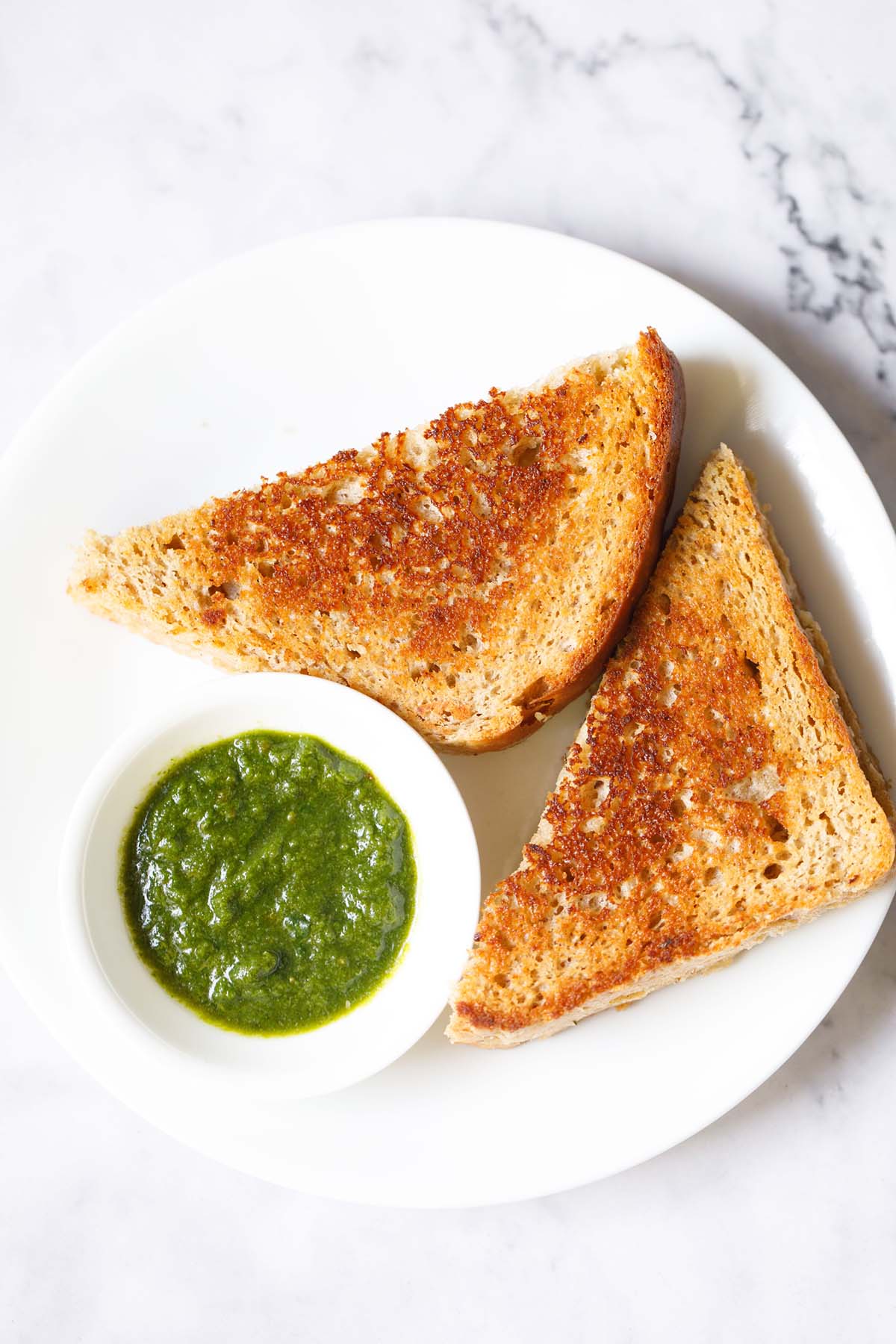 overhead shot of cheese sandwich triangle slices with cilantro dip on a white plate