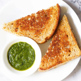 overhead shot of cheese sandwich triangle slices with cilantro dip on a white plate