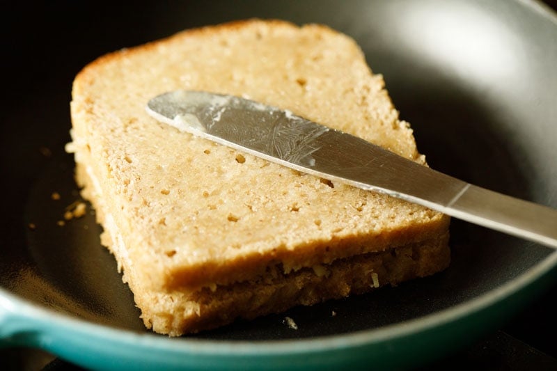 butter being spread on the top bread of the cheese sandwich in the pan