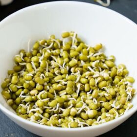 moong sprouts in a white bowl placed on dark gray slate board.