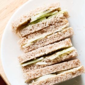 close up shot of stacked cucumber sandwiches with the visible layers of cucumber and bread placed on a white plate.