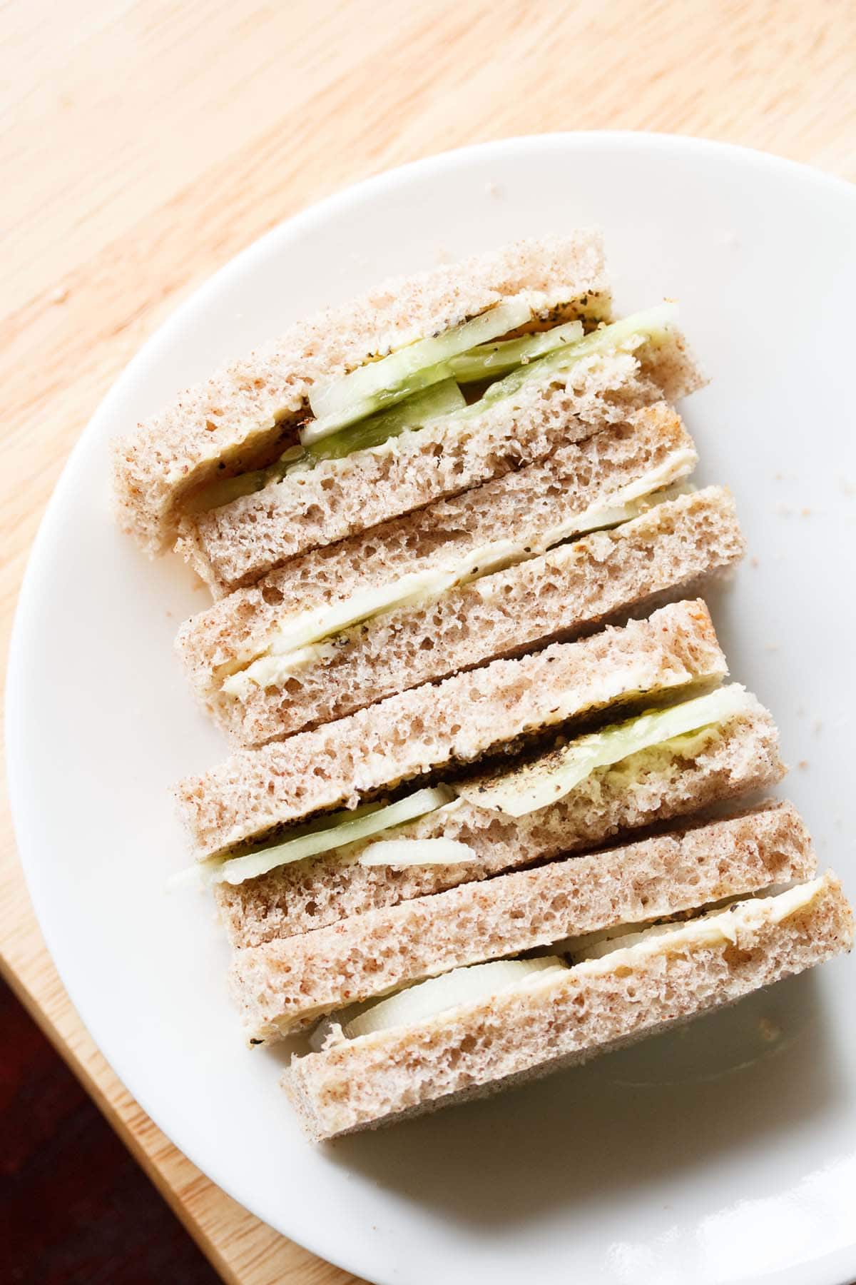 close up shot of stacked cucumber sandwiches with the visible layers of cucumber and bread placed on a white plate.