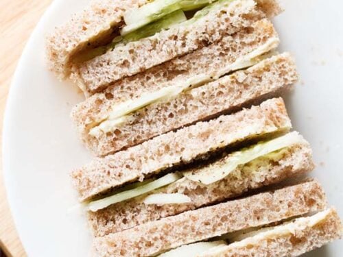 close up shot of stacked cucumber sandwiches with the visible layers of cucumber and bread placed on a white plate.