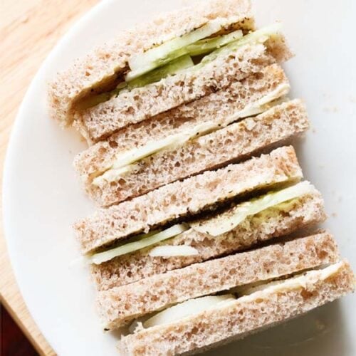 close up shot of stacked cucumber sandwiches with the visible layers of cucumber and bread placed on a white plate.