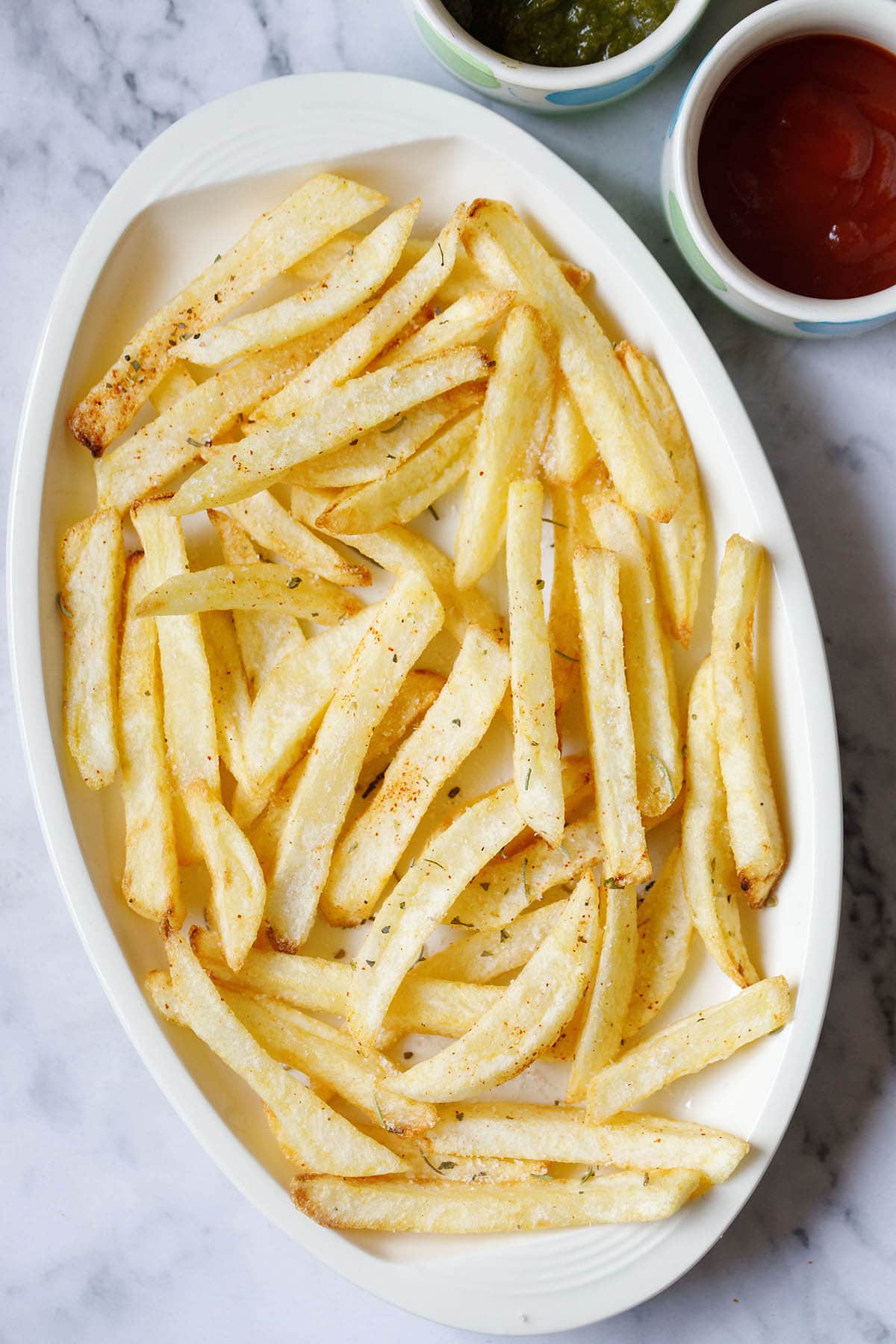 overhead shot of a bowlful of homemade seasoned french fries with dipping sauces