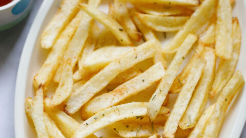 white serving tray filled with homemade french fries next to small dipping bowls of ketchup and green chutney