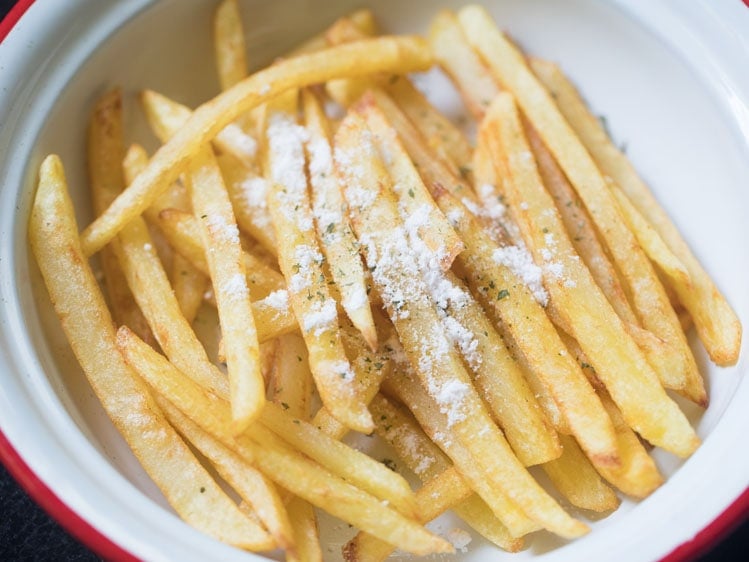 adding herbs, seasonings to french fries in a bowl