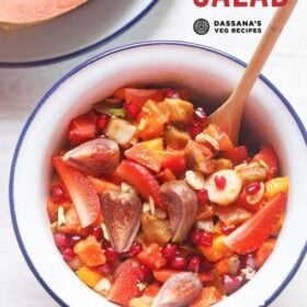 figs, strawberries, bananas, mango, chikoo, papaya and pomegranate tropical fruit salad in a white bowl next to a halved papaya