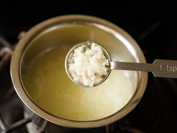 garlic being added with a 1 teaspoon measuring bowl to melted butter