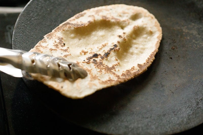 slightly charred and cooked side of naan held with tongs on the skillet