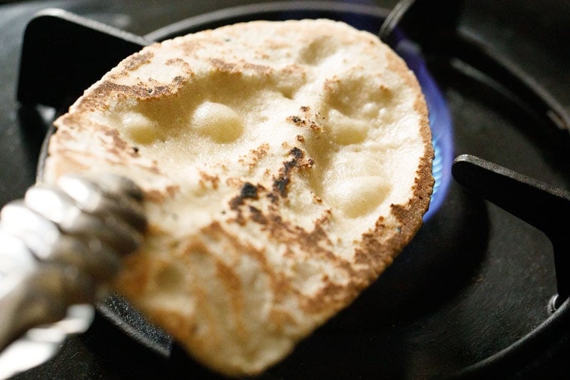 garlic naan held with tongs and placed on stove-top flame