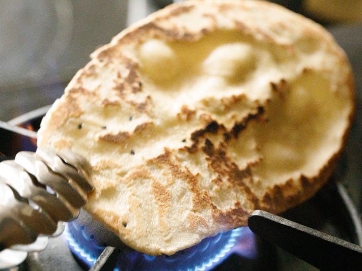 garlic naan being roasted on stove-top flame