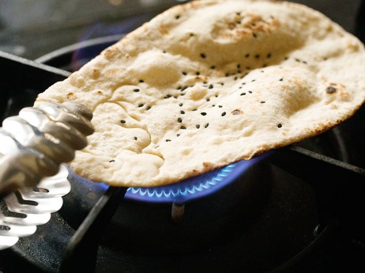 garlic naan being roasted on stove-top flame