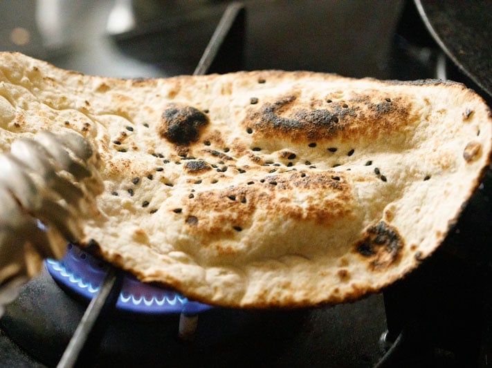garlic naan being roasted on stove-top flame