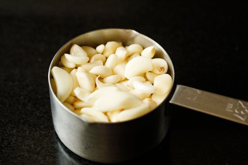 peeled garlic cloves in a silver measuring cup