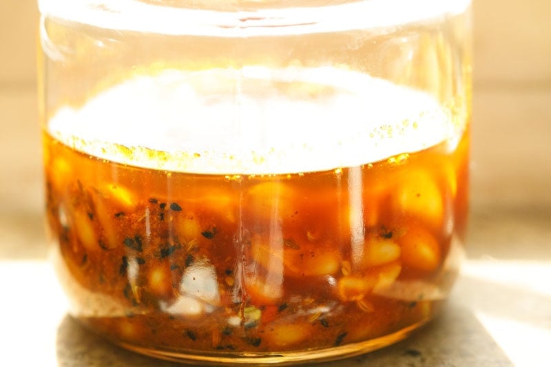 jar of garlic pickles in a sunny window for infusing the achaar