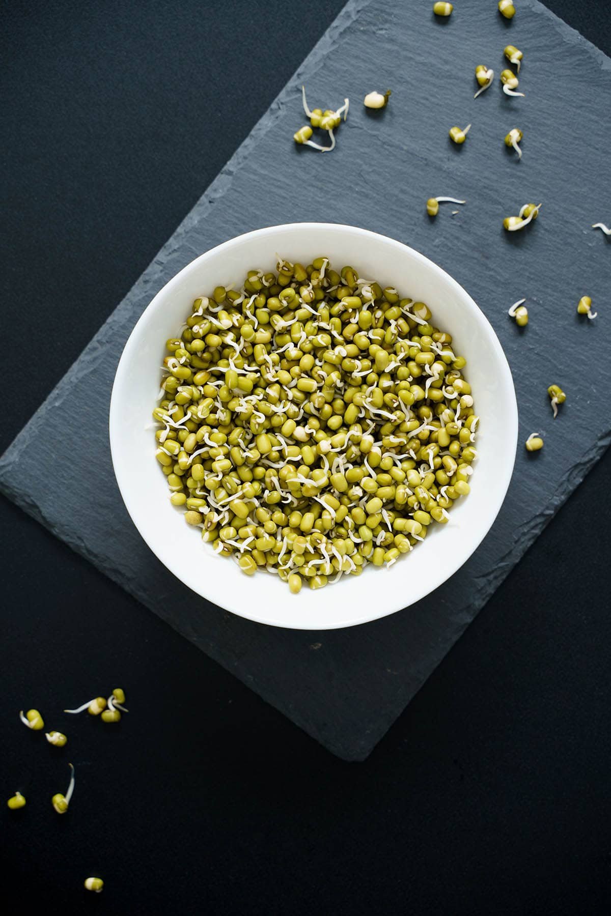 green gram sprouts in a white bowl on a gray slate board on a black board