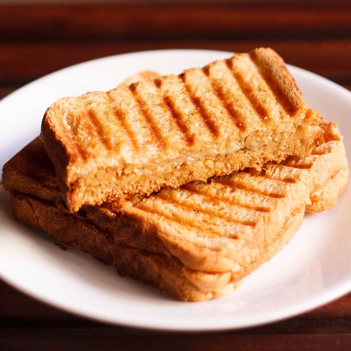 cheese sandwiches on a white plate on a dark brown table