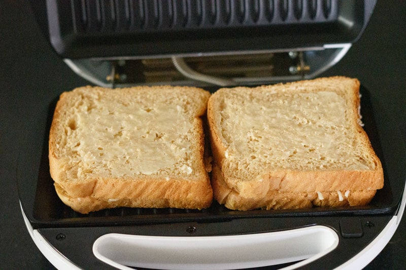 two cheese sandwich placed in a grill with butter spread on top of the bread
