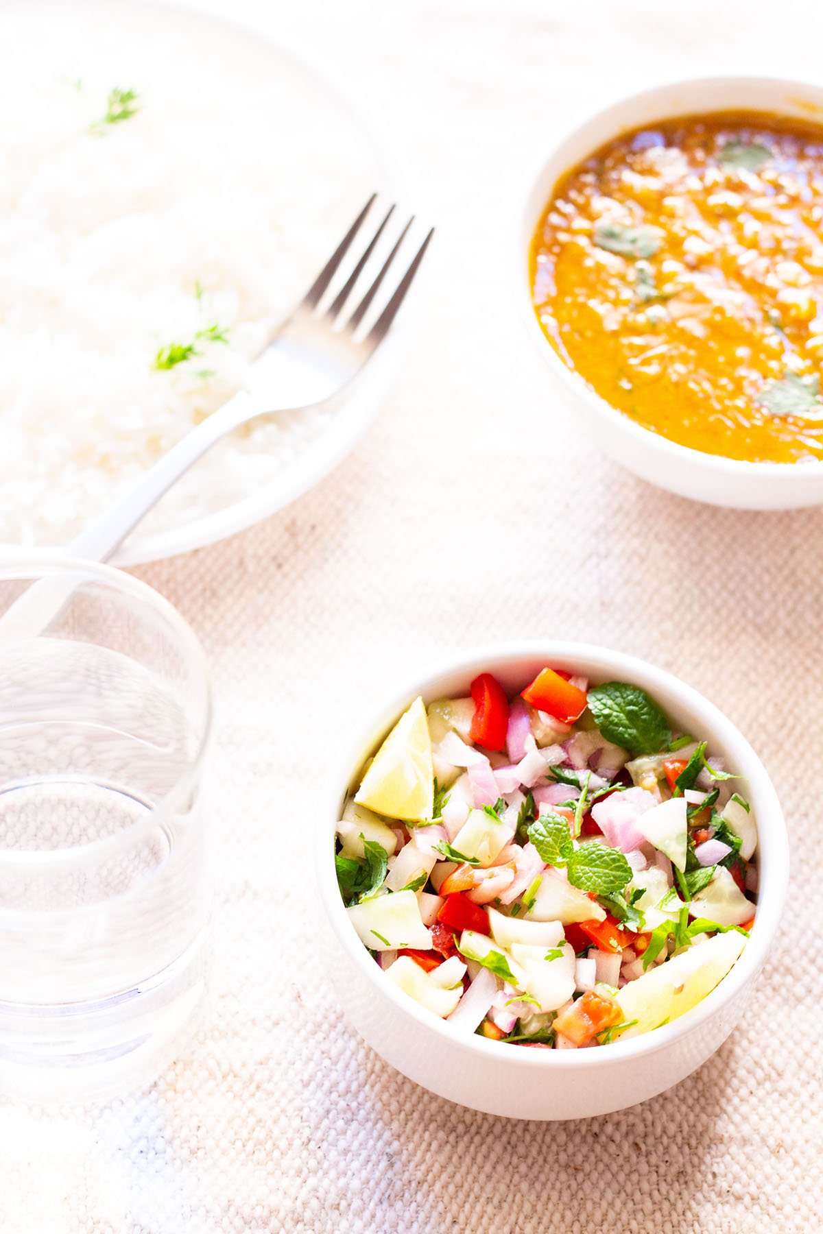 kachumber salad in a small white bowl on a table next to bowls of rice and curry