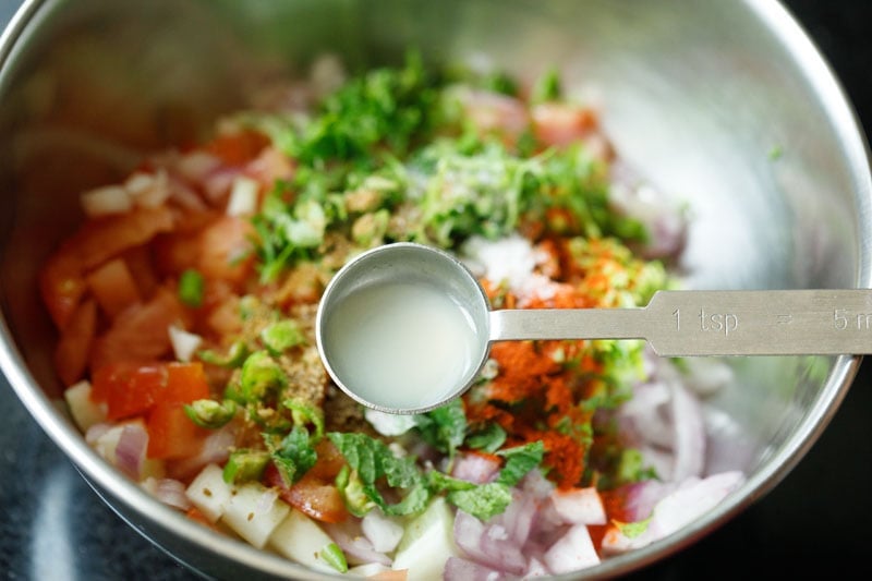 teaspoon with lemon juice above bowl of chopped veggies for kachumber salad recipe