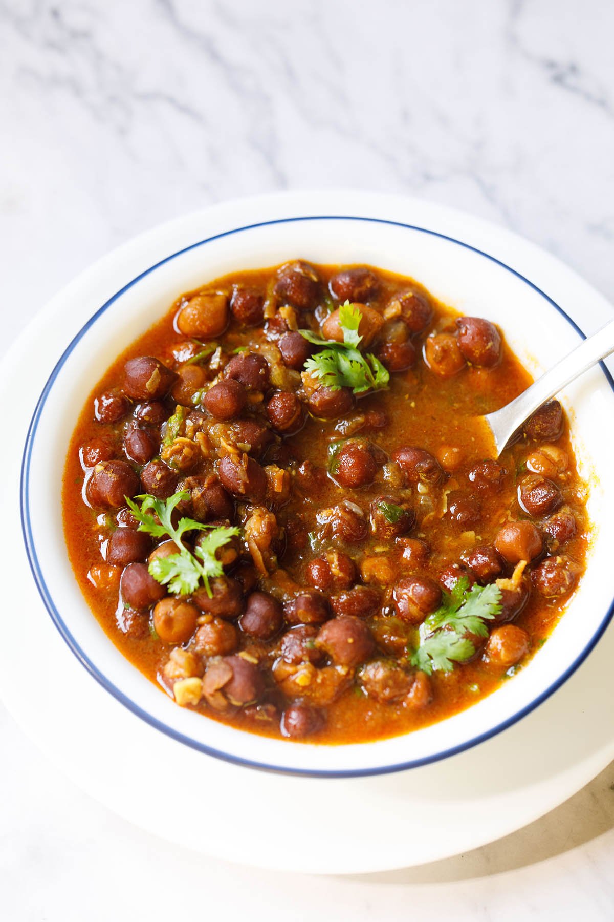 kala chana curry with a silver spoon in a blue rimmed bowl