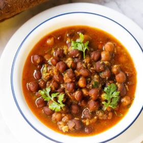 overhead shot of kala chana gravy with three coriander sprigs on top in a blue rimmed white bowl