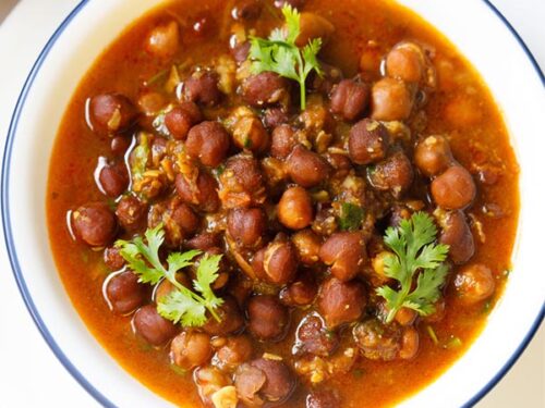 kala chana gravy with three coriander sprigs on top in a blue rimmed white bowl