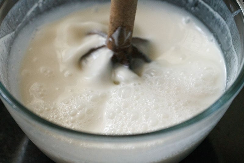 curd mixture being churned with wooden churner to make lassi