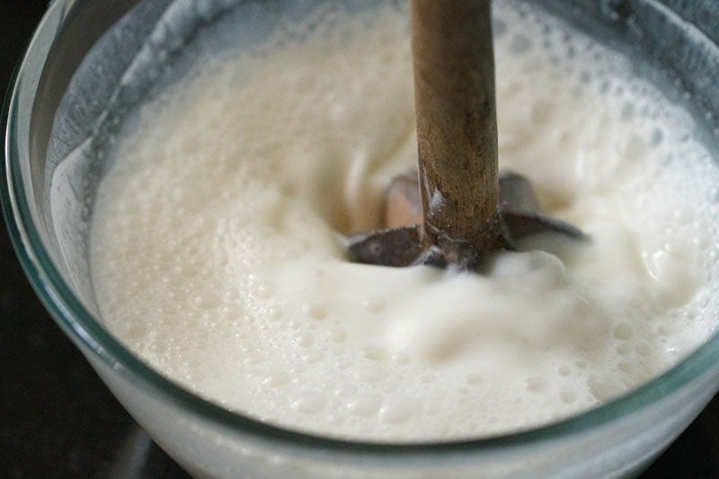 curd, water and sugar being blended and churned with handheld wooden churner