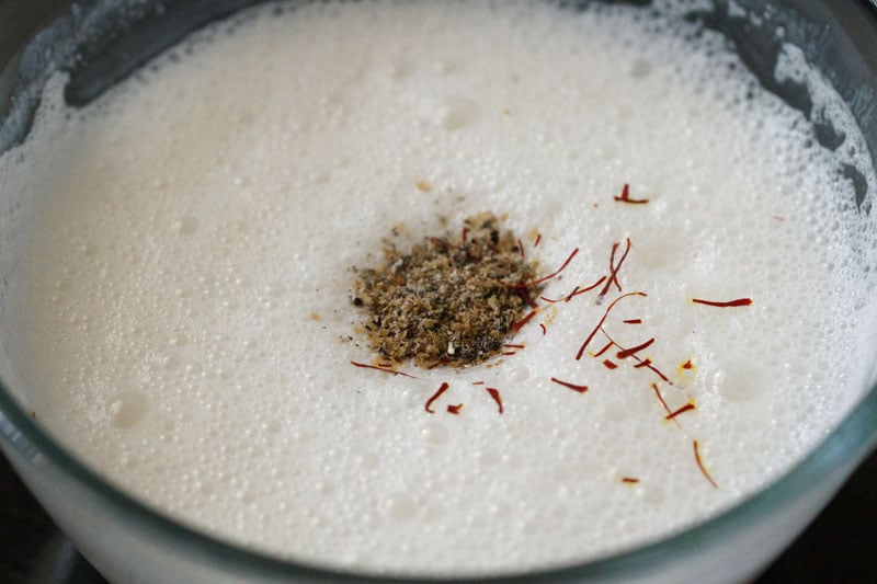 cardamom powder and saffron strands on top of the frothy lassi