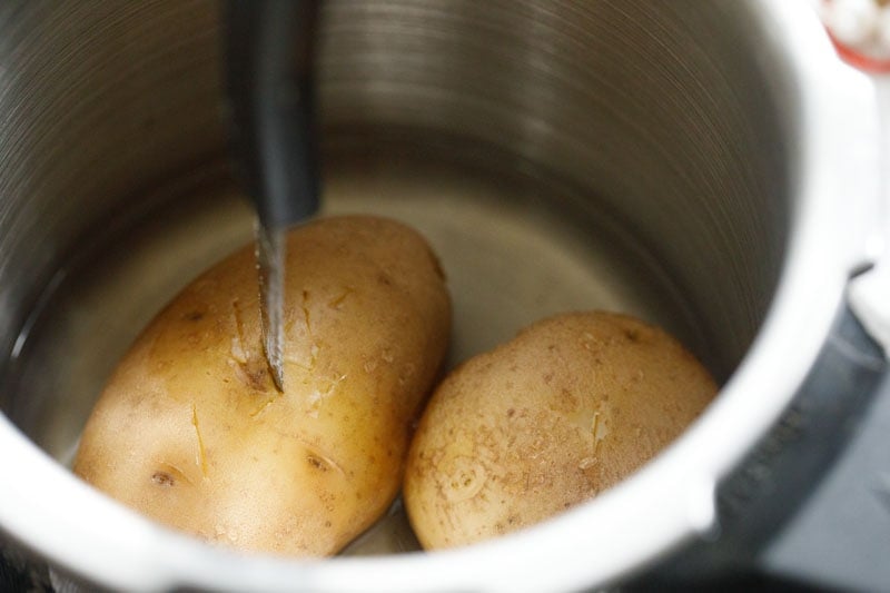 two boiled potatoes in a pressure cooker with a knife inserted in one potato to check the doneness