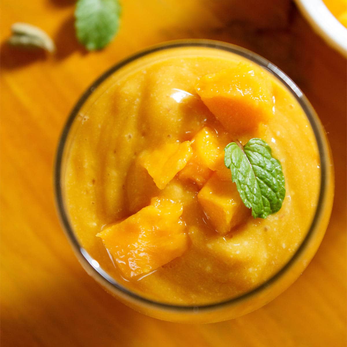 mango smoothie with almonds in a glass topped with some chopped mangoes and a mint leaf