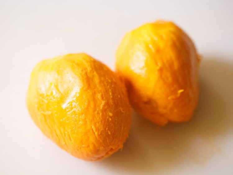 two peeled mangoes on a white chopping board