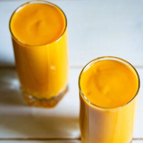 batido de mango en dos vasos altos sobre una mesa blanca