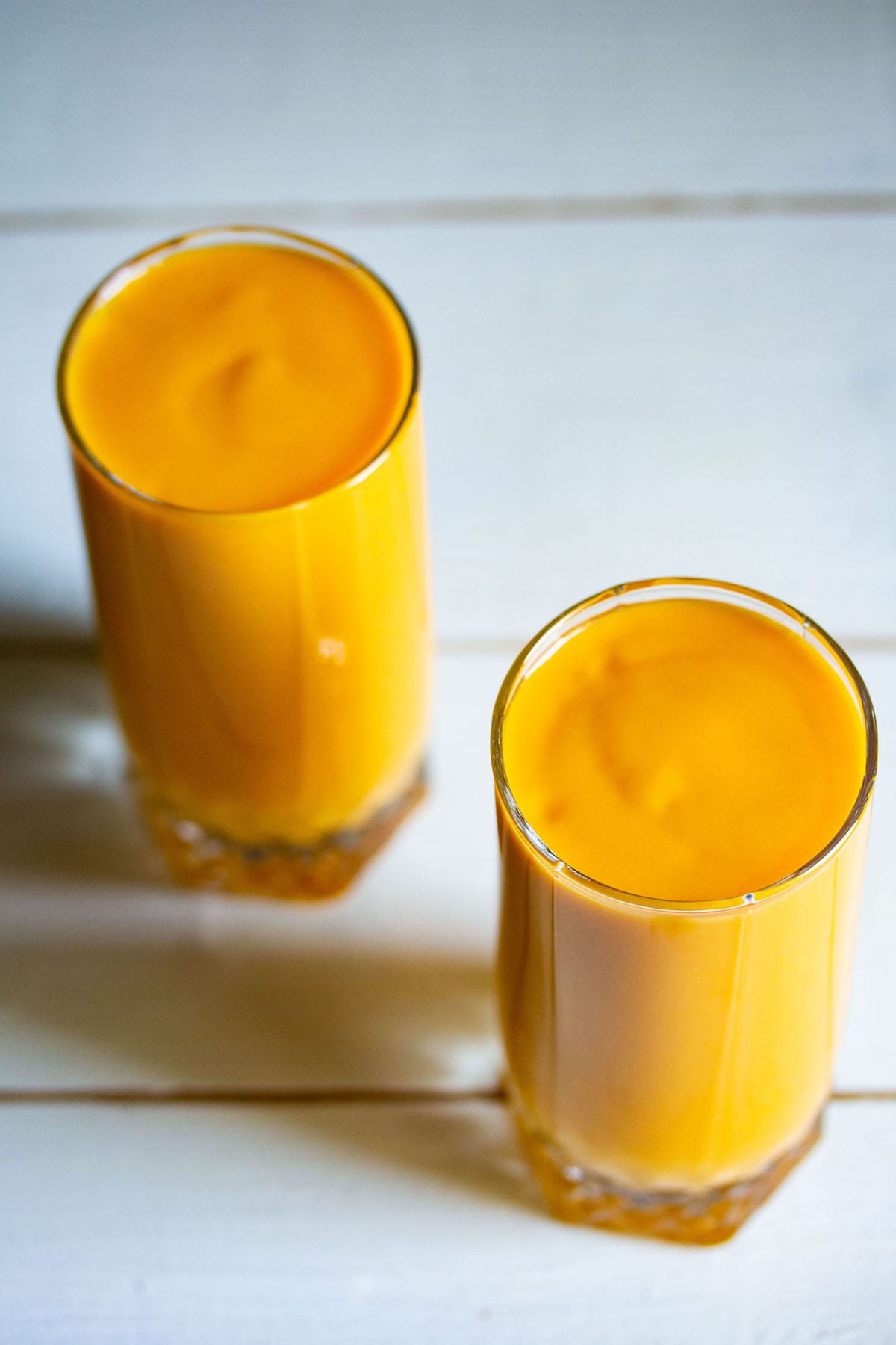 mango milkshake in two tall glasses on a white table